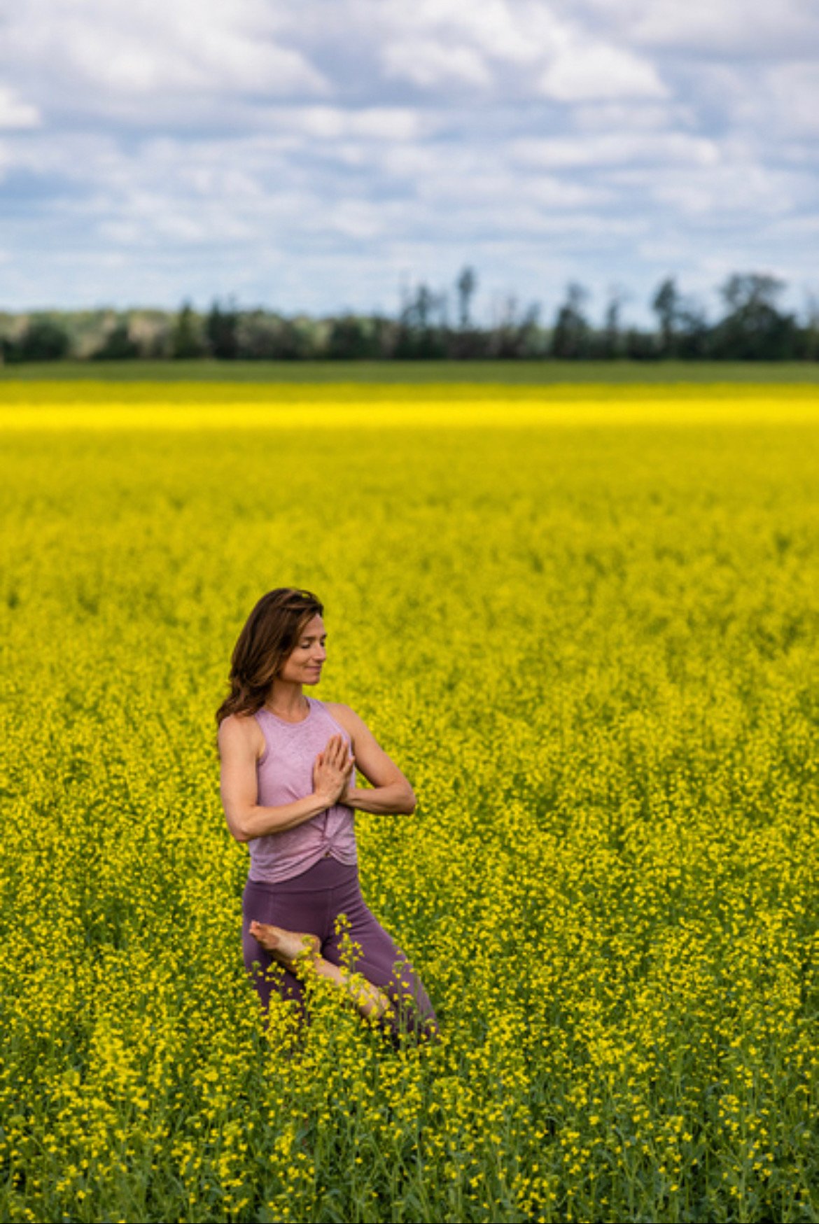 Sam Manchulenko holding tree pose with handing in prayer position standing in a yellow green field