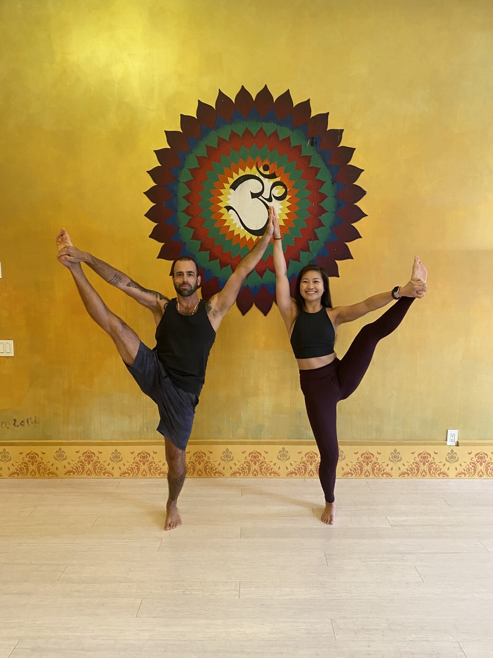 Jerome Burdi and Jessica Hwang holding ballet pose in from of vibrant om symbol