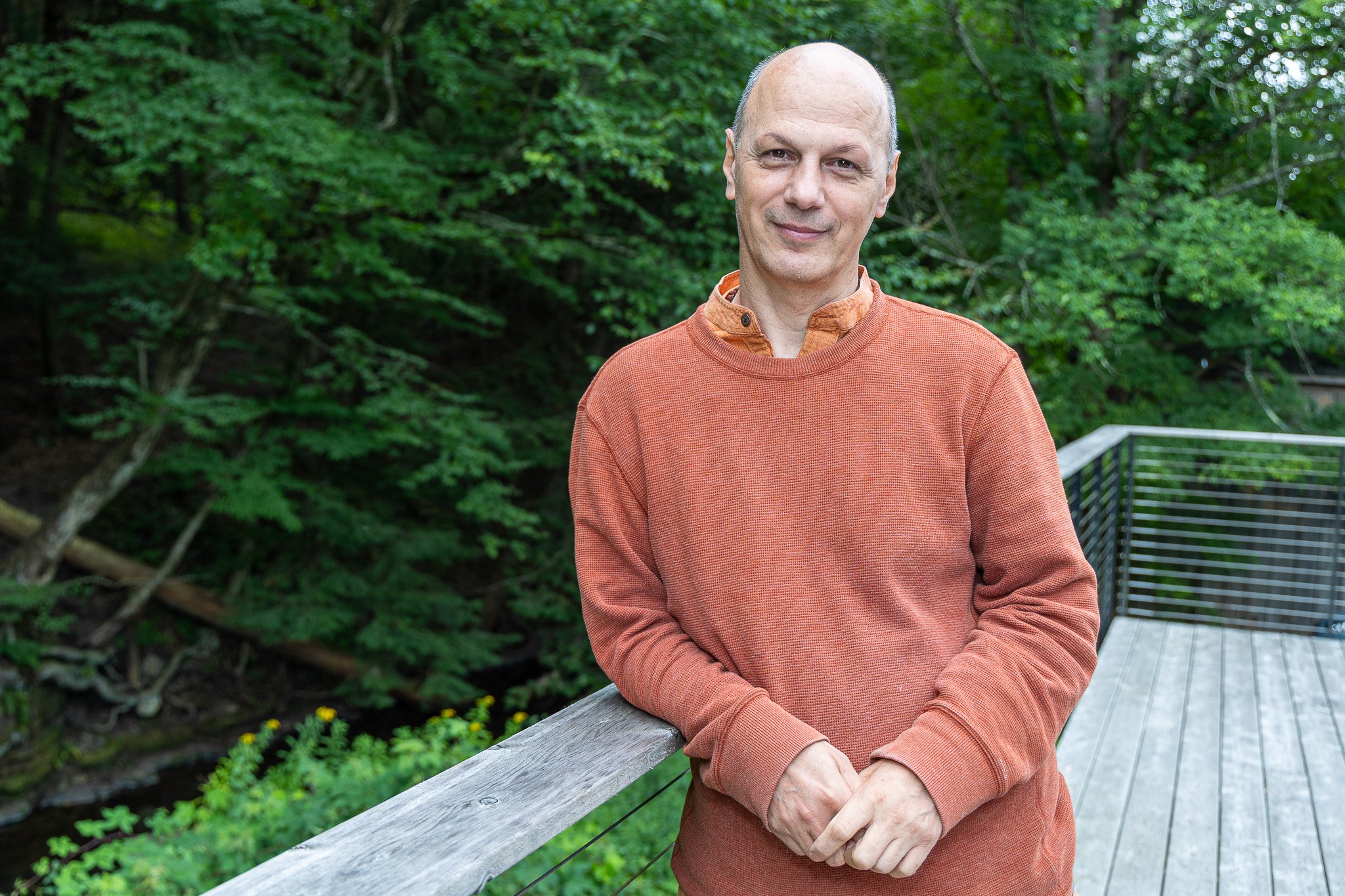 former monk and yoga teacher Prem Sadasivananda casually leaning against a wooden railing with a backdrop of lush trees