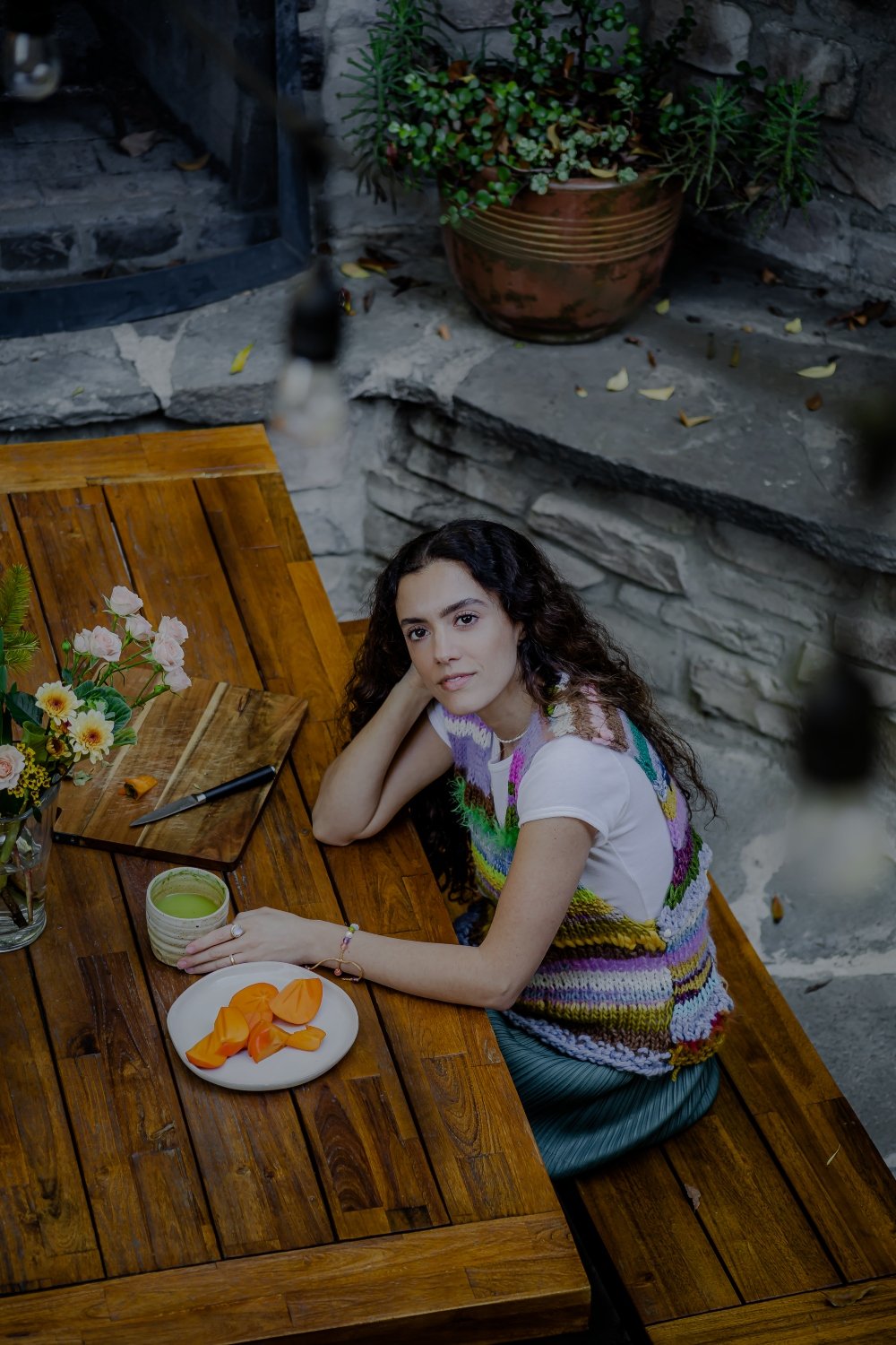Tonya Papanikolov enjoying a healthy breakfast, holding a cup of matcha tea at a wooden table, with a plate of fresh food in front of her.