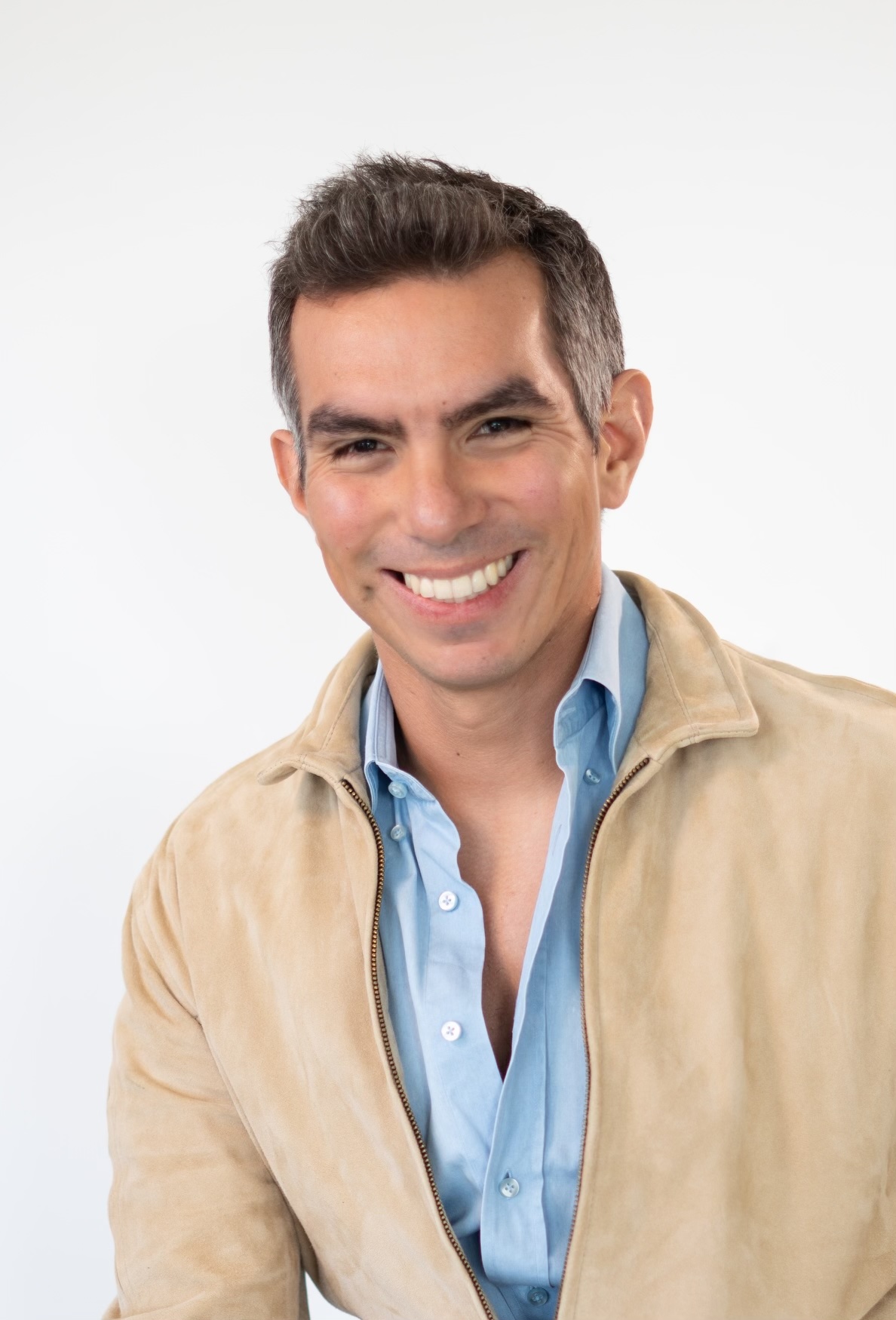 Renzo del Castillo in a blue shirt and tan jacket