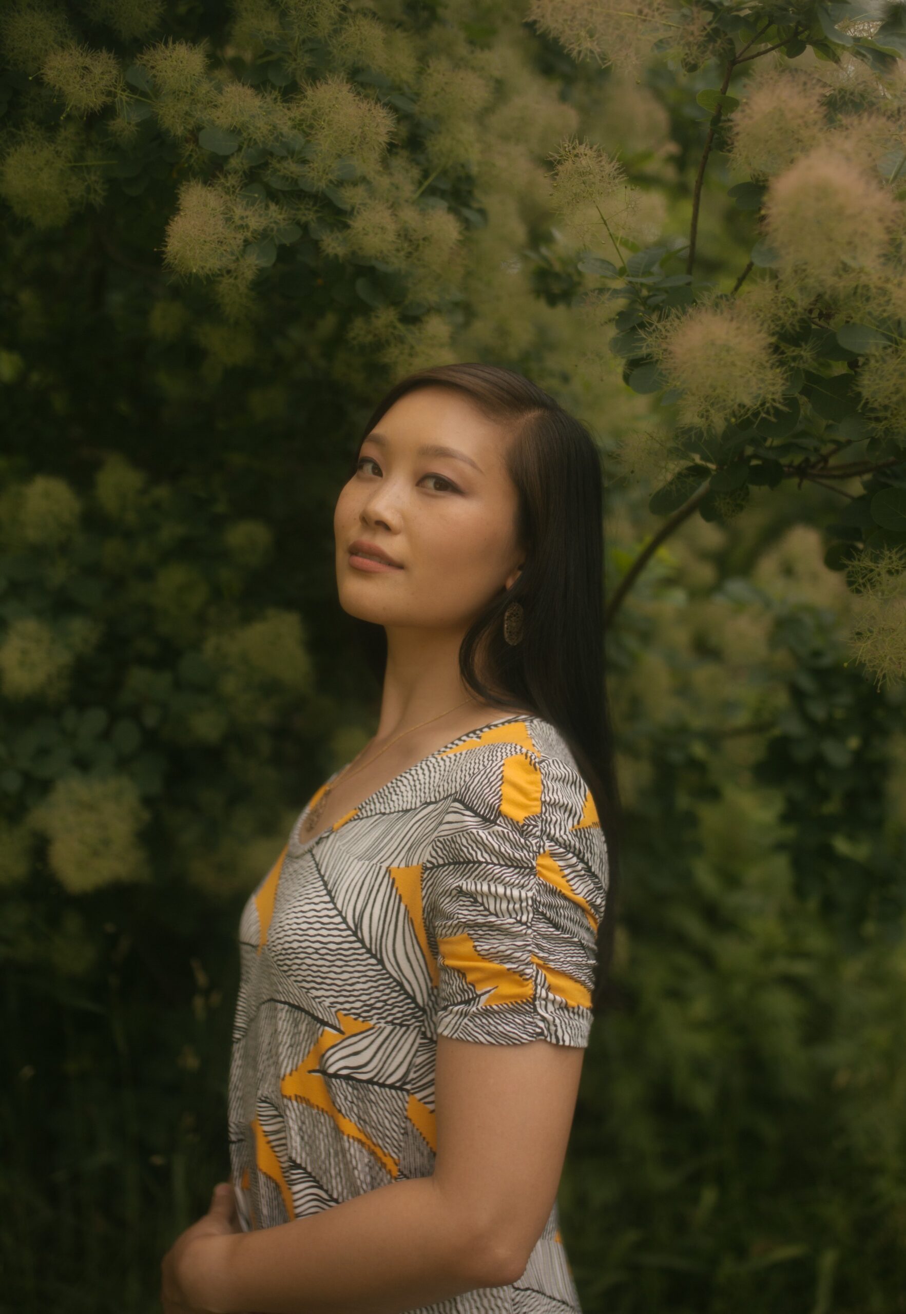 Jessica Hwang in a black, white, and yellow dress in front of a beautiful tree with soft yellow flowers