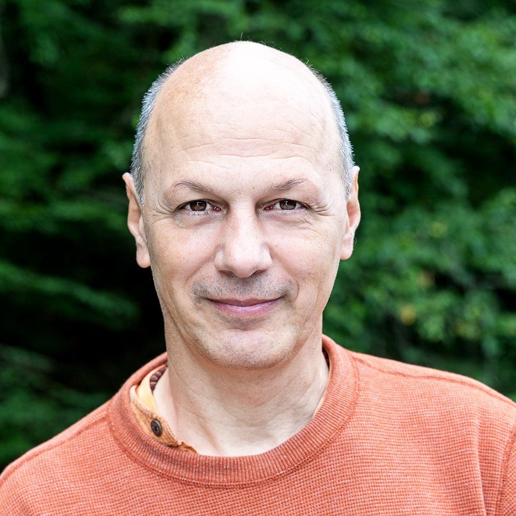 Prem Sadasivananda standing in an orange shirt in front of trees