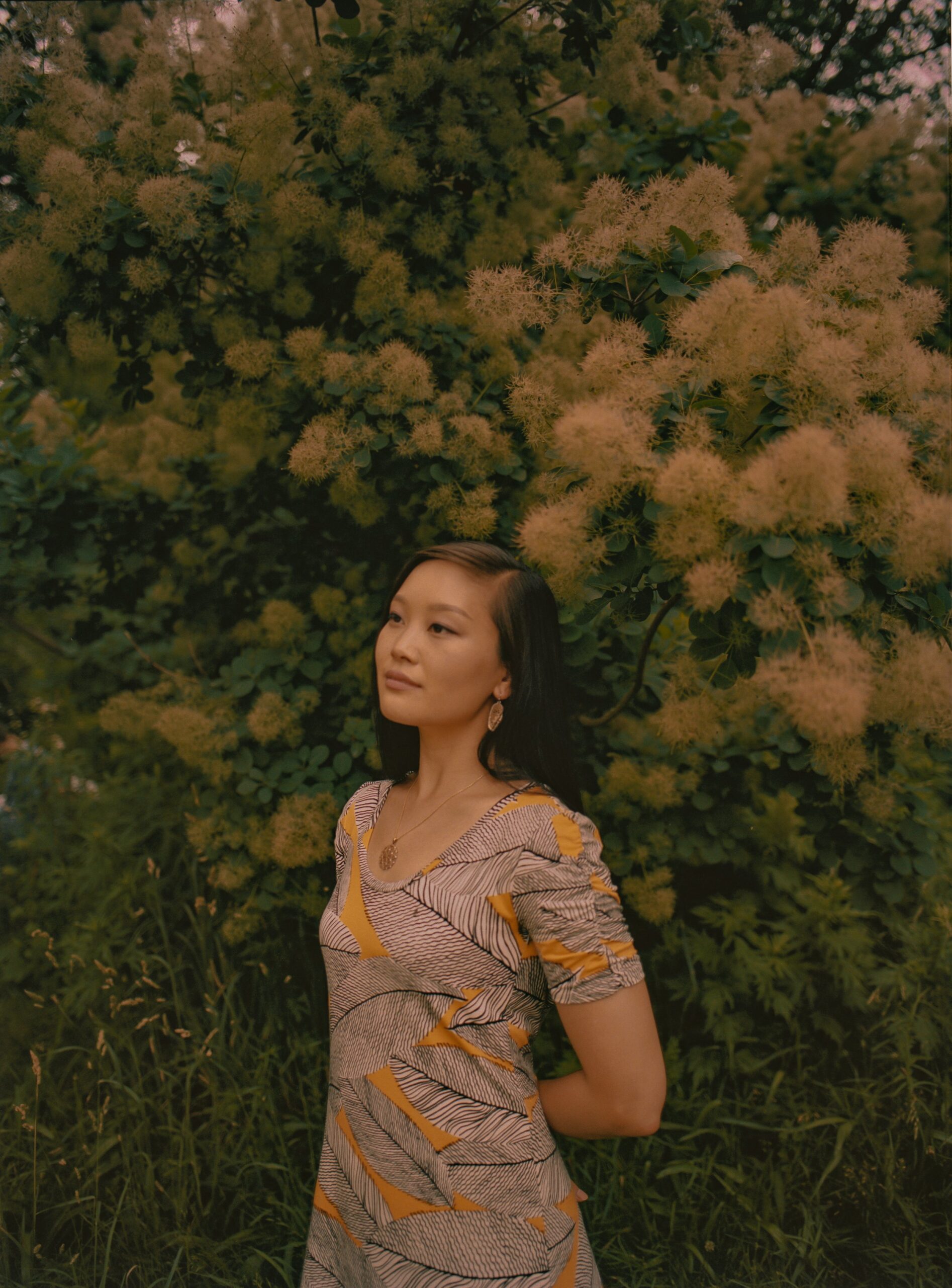 Jessica Hwang standing in a dress in front of a large tree with yellow flowers