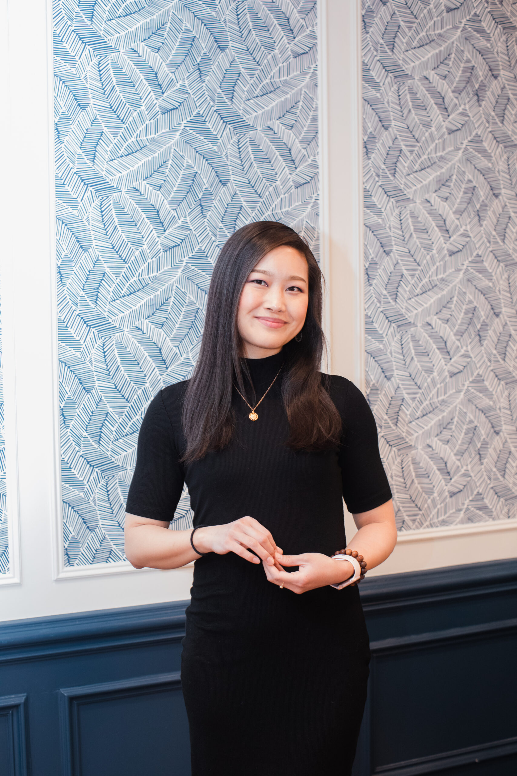 Jessica Hwang in a black dress standing in front of a blue patterned wall