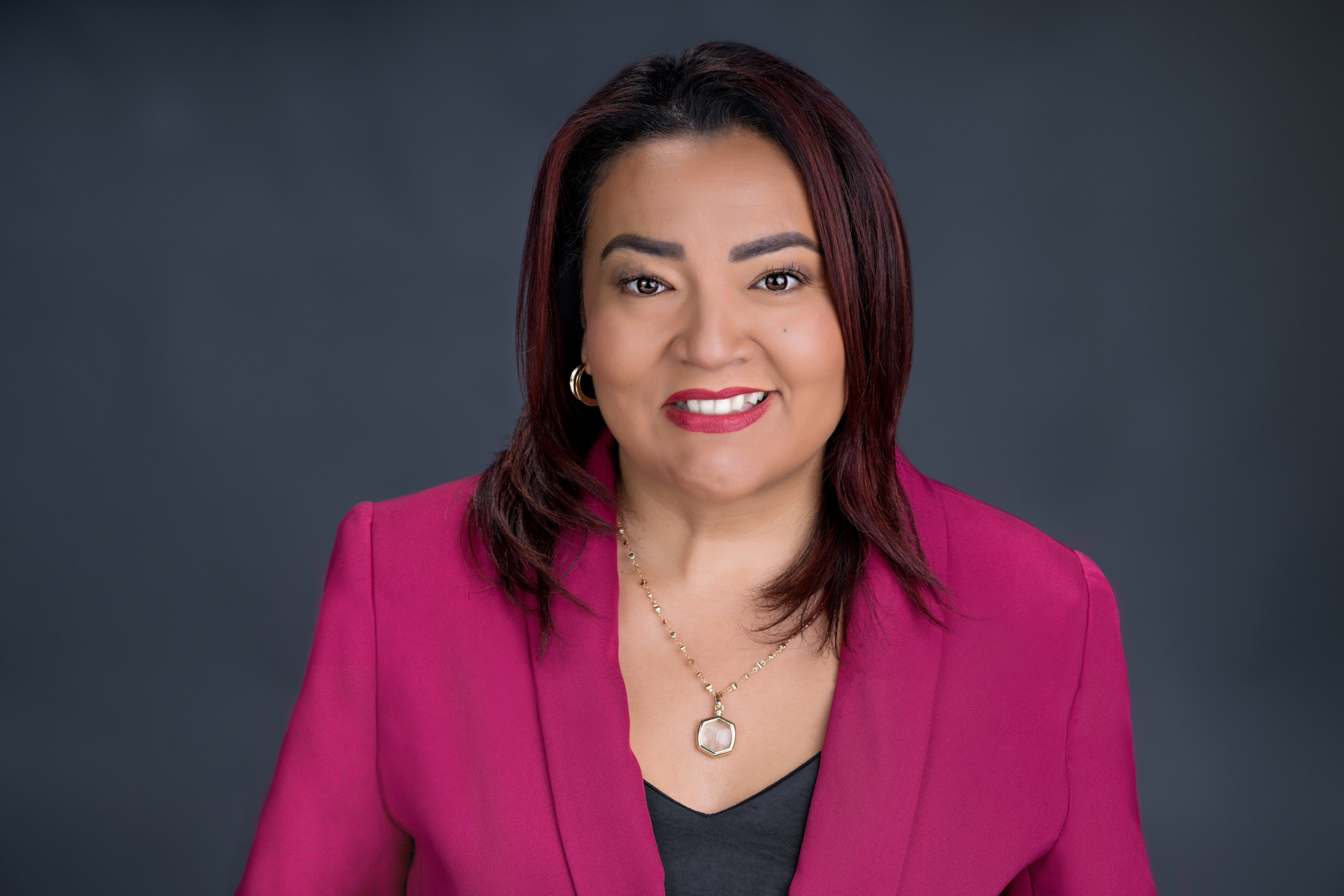 Sugey Piedra smiling in a magenta jacket and black top