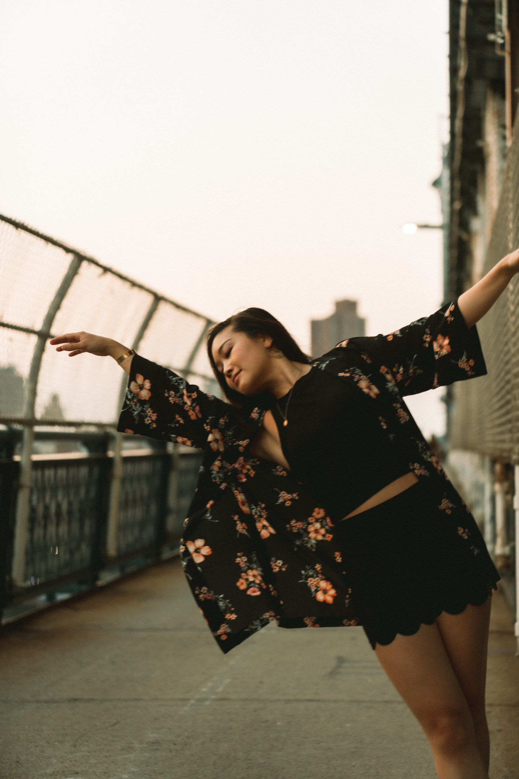 Jessica Hwang in a black and floral outfit with arms outstretched on Manhattan Bridge